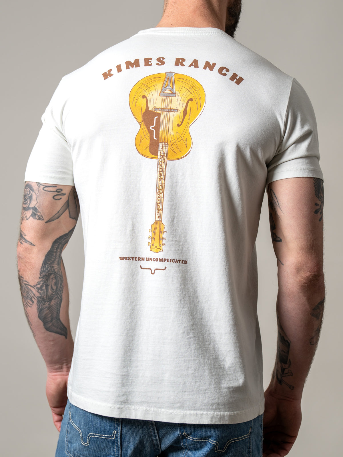 Kimes Ranch Lucky B Tuned shirt in Natural, back view, with a back graphic of a yellow acoustic guitar with Kimes Ranch