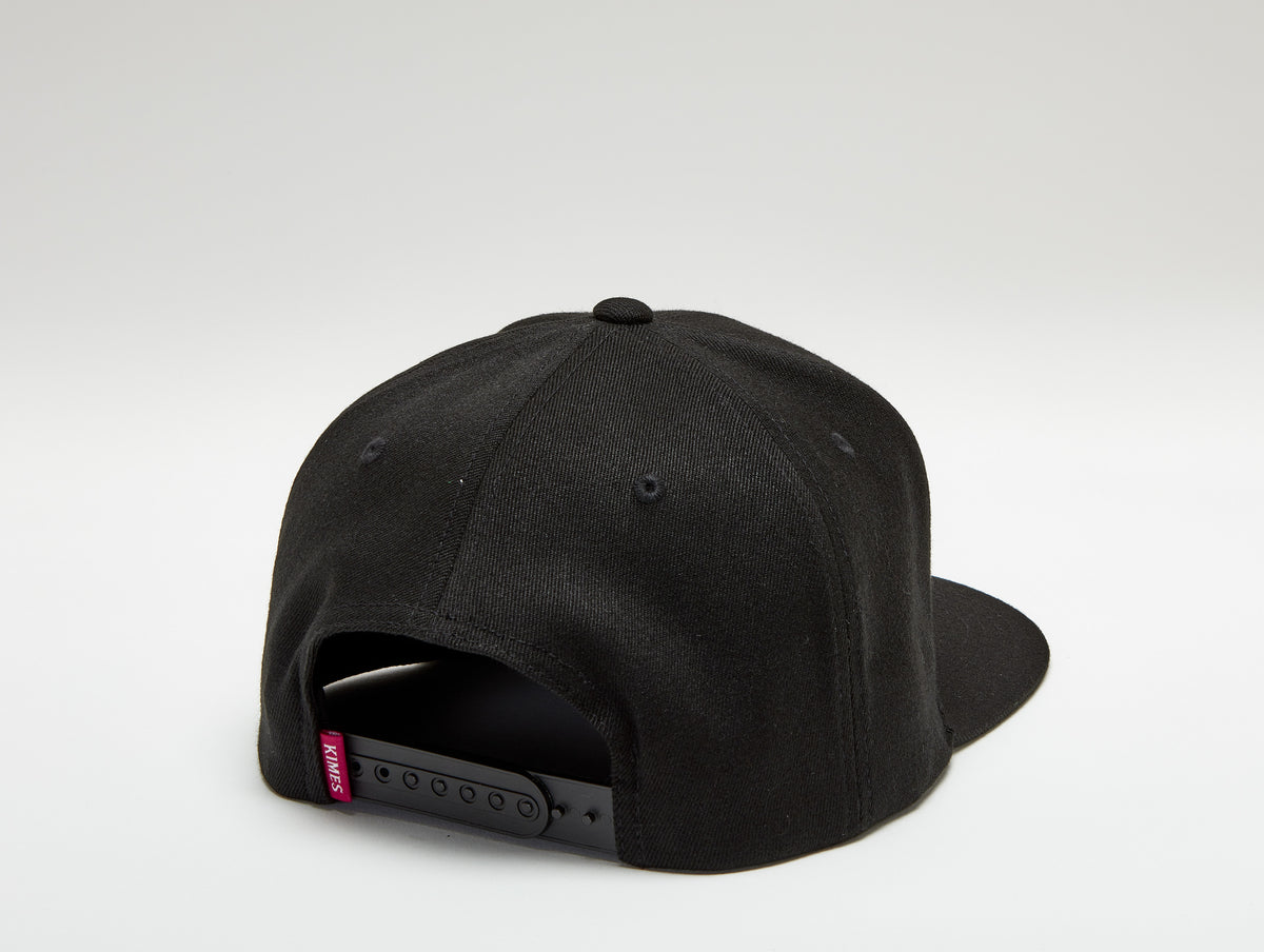Kimes Ranch Arched Trucker Hat in Black, back view, with the adjustable strap closure and red Kimes Ranch logo tab