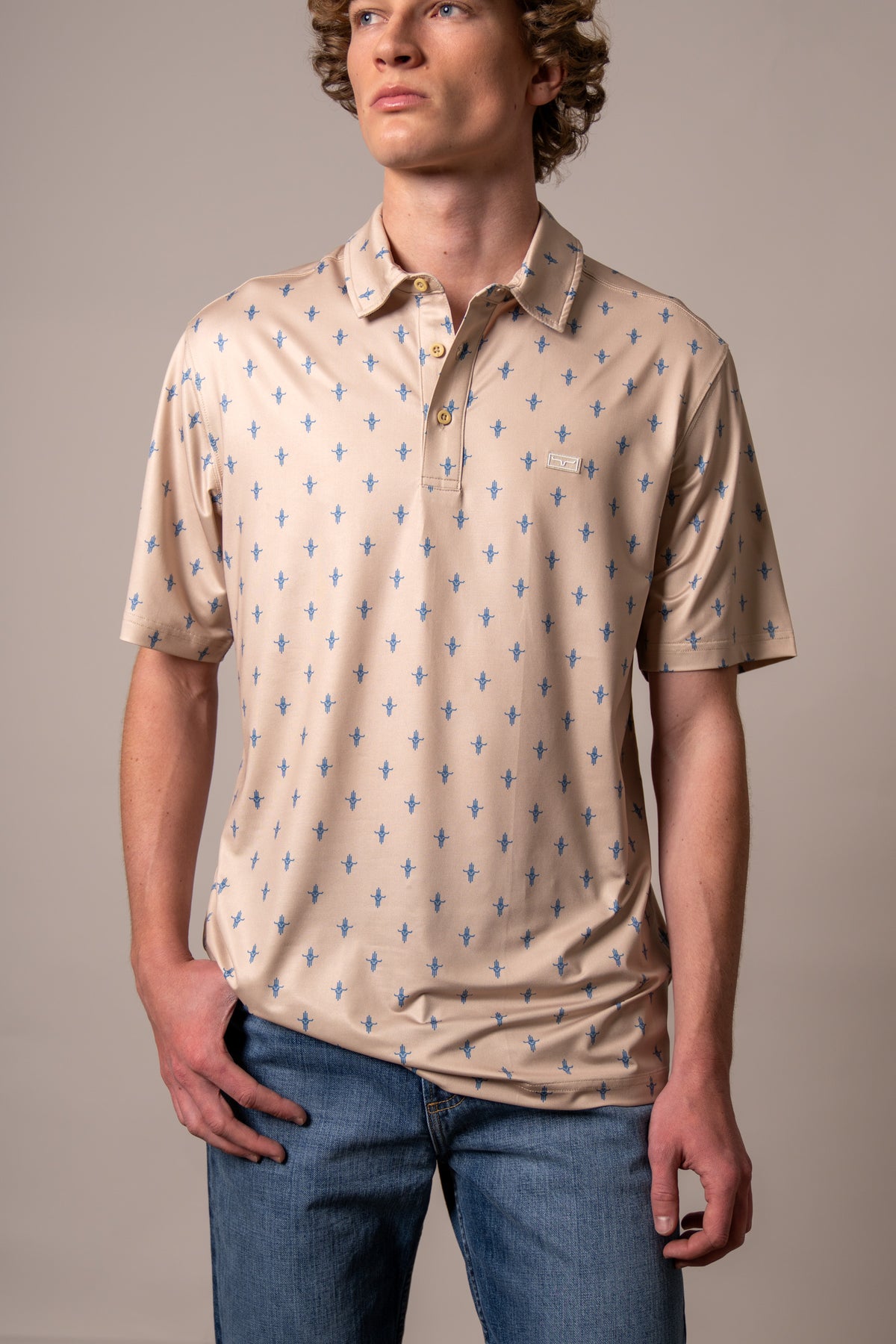Kimes Ranch Bartram polo in Natural with a repeating blue steer logo pattern and a chest logo patch
