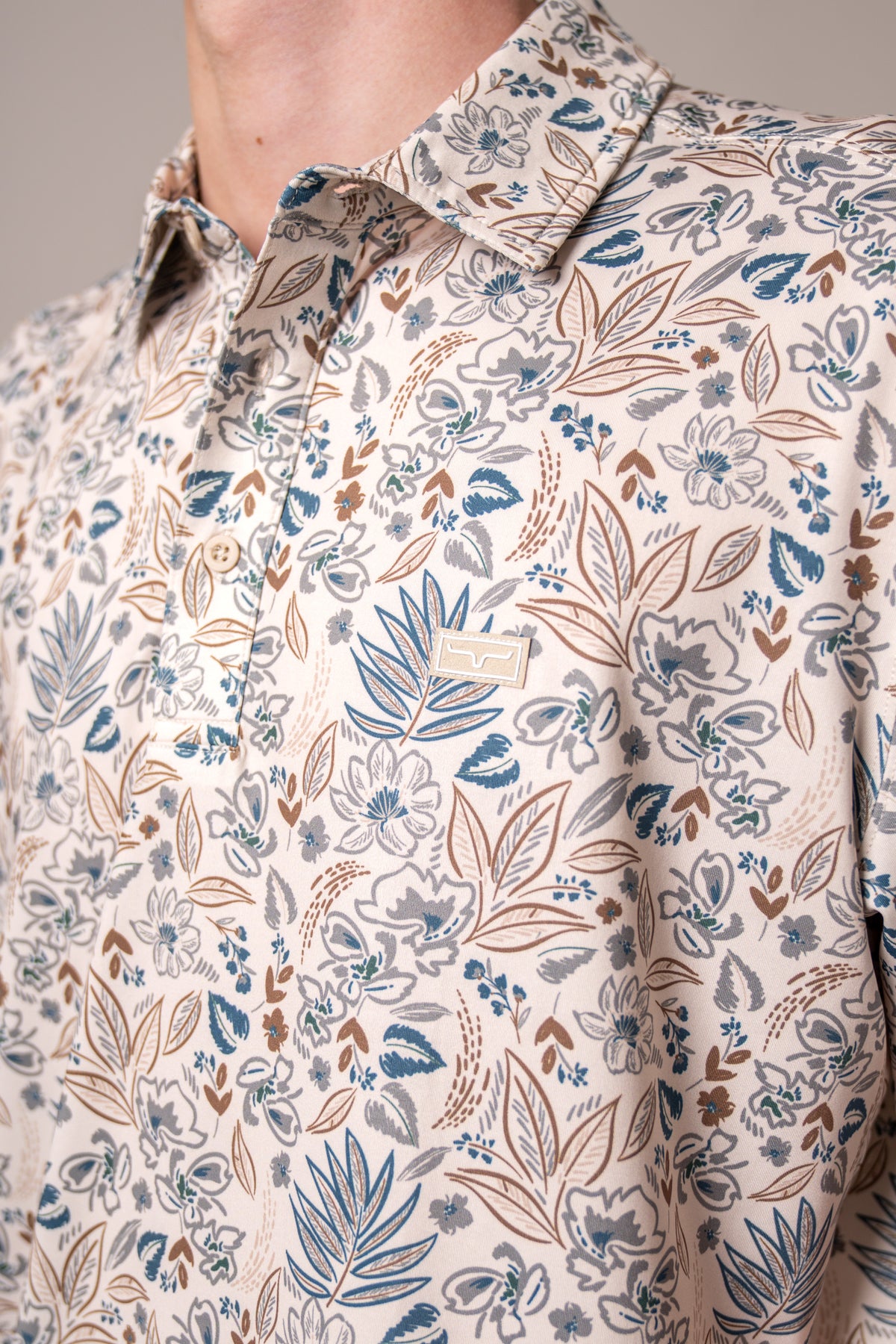 Kimes Ranch Bartram polo in Stone, close-up, with a blue and brown floral print and a logo patch