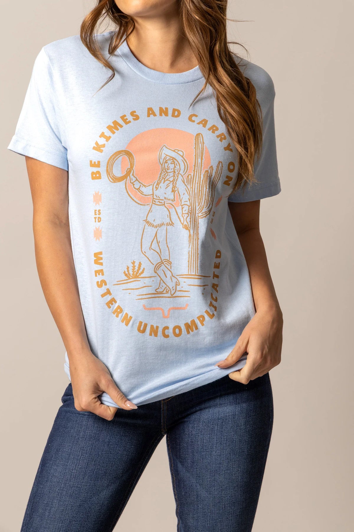 Kimes Ranch Be Kimes shirt in Baby Blue with a graphic of a cowgirl and the text Be Kimes and Carry On Western Uncomplicated