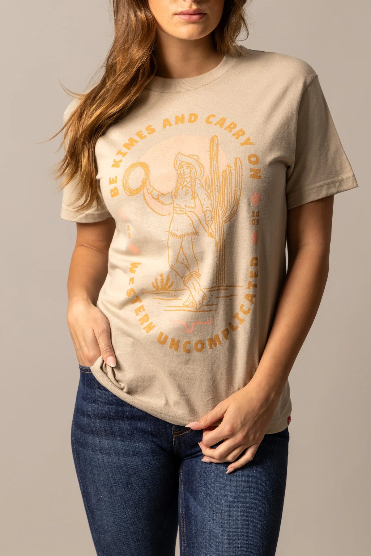Kimes Ranch Be Kimes shirt in Sand with a graphic of a woman in a cowboy hat and text reading Be Kimes