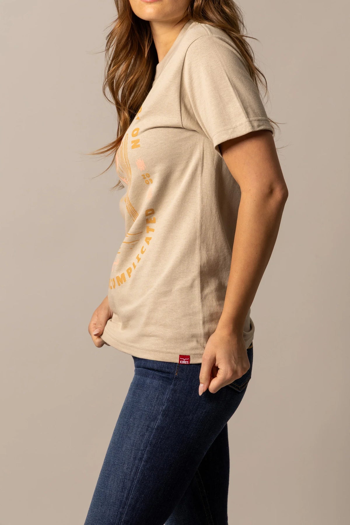 Kimes Ranch Be Kimes shirt in Sand, side view, with the graphic print and red Kimes Ranch logo tag
