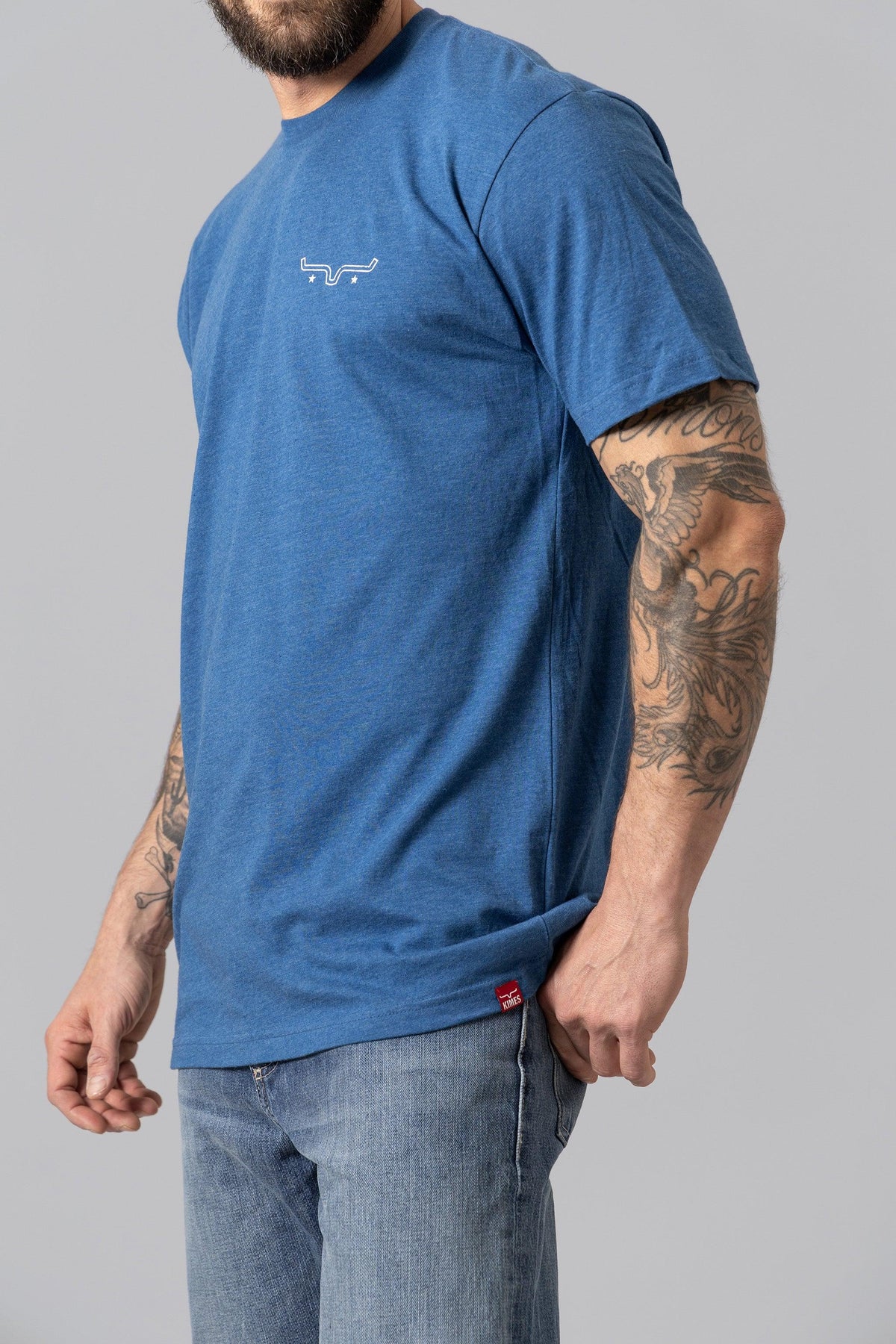 Kimes Ranch American Bullseye Shirt in Heather Cool Blue, side view, with a white logo on the chest and a red tag at the hem
