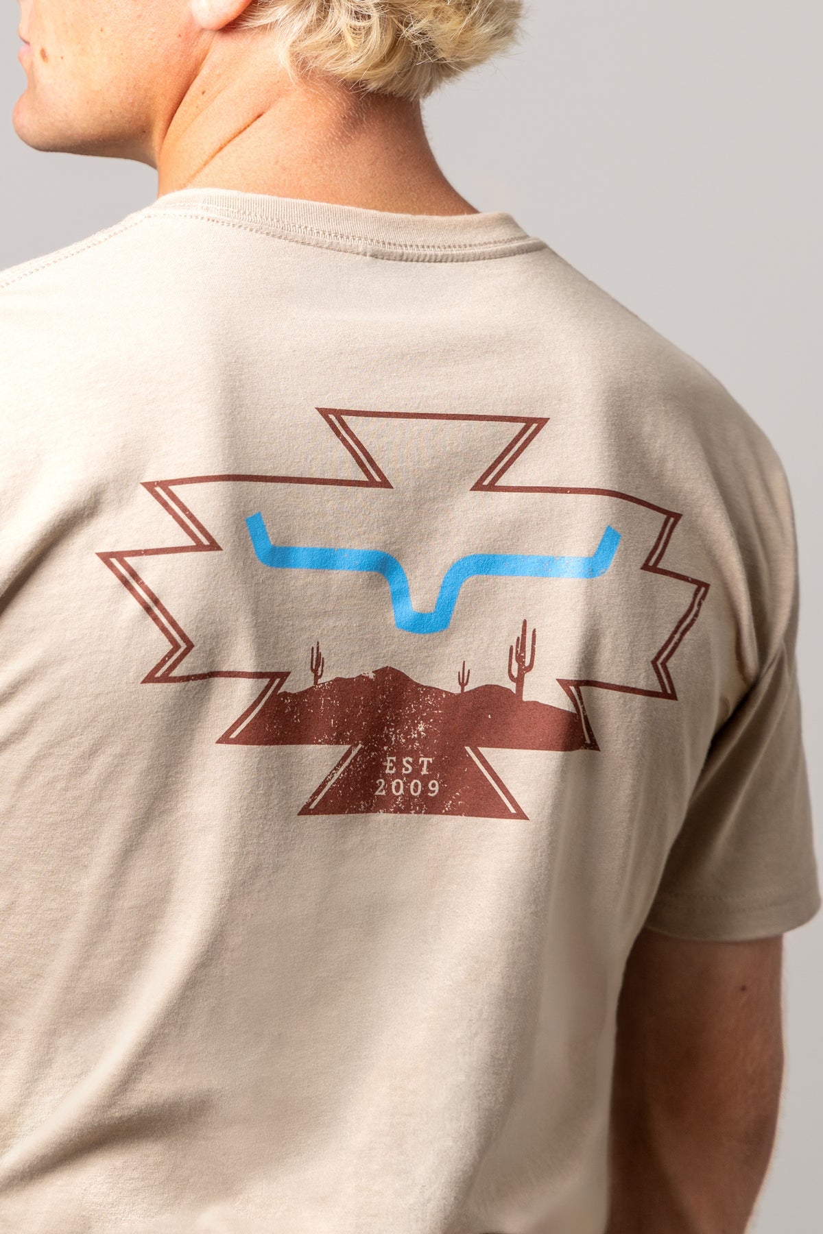 Kimes Ranch Long Live shirt in Tan, back view, with a back graphic of the Kimes Ranch logo with cacti and EST 2009