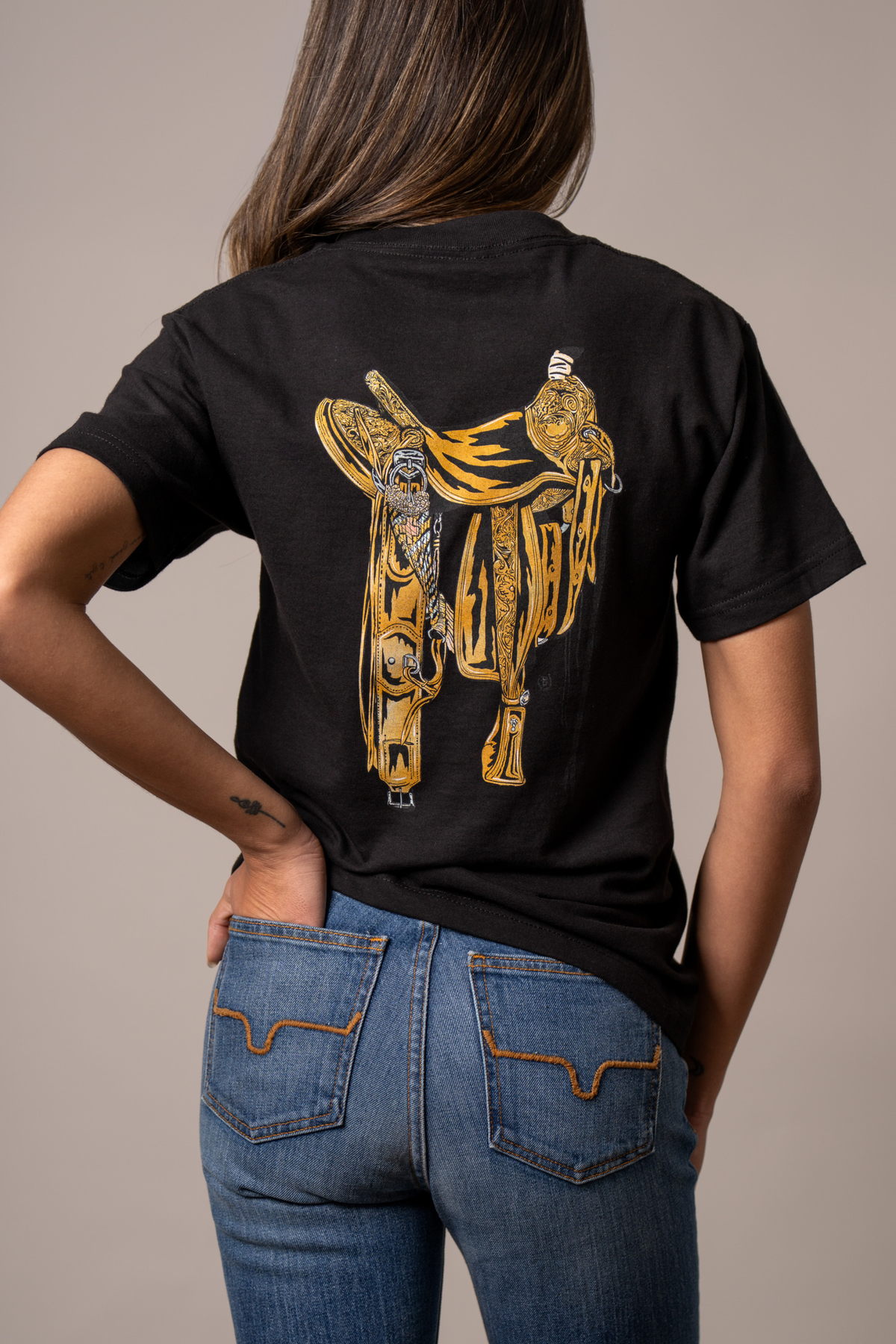 Kimes Ranch Lucky B Saddle, back view, Black shirt with a large gold western saddle graphic on the back