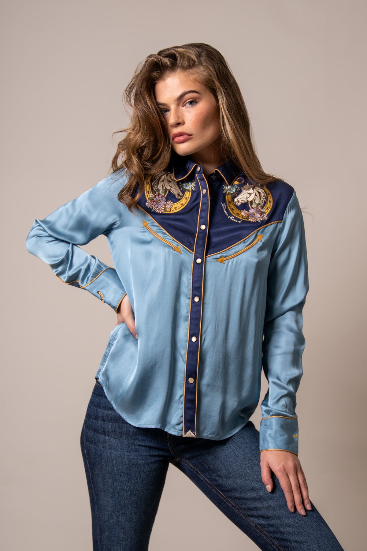 Kimes Ranch Merada top in Mid Blue with embroidered horse heads on the yoke and gold piping