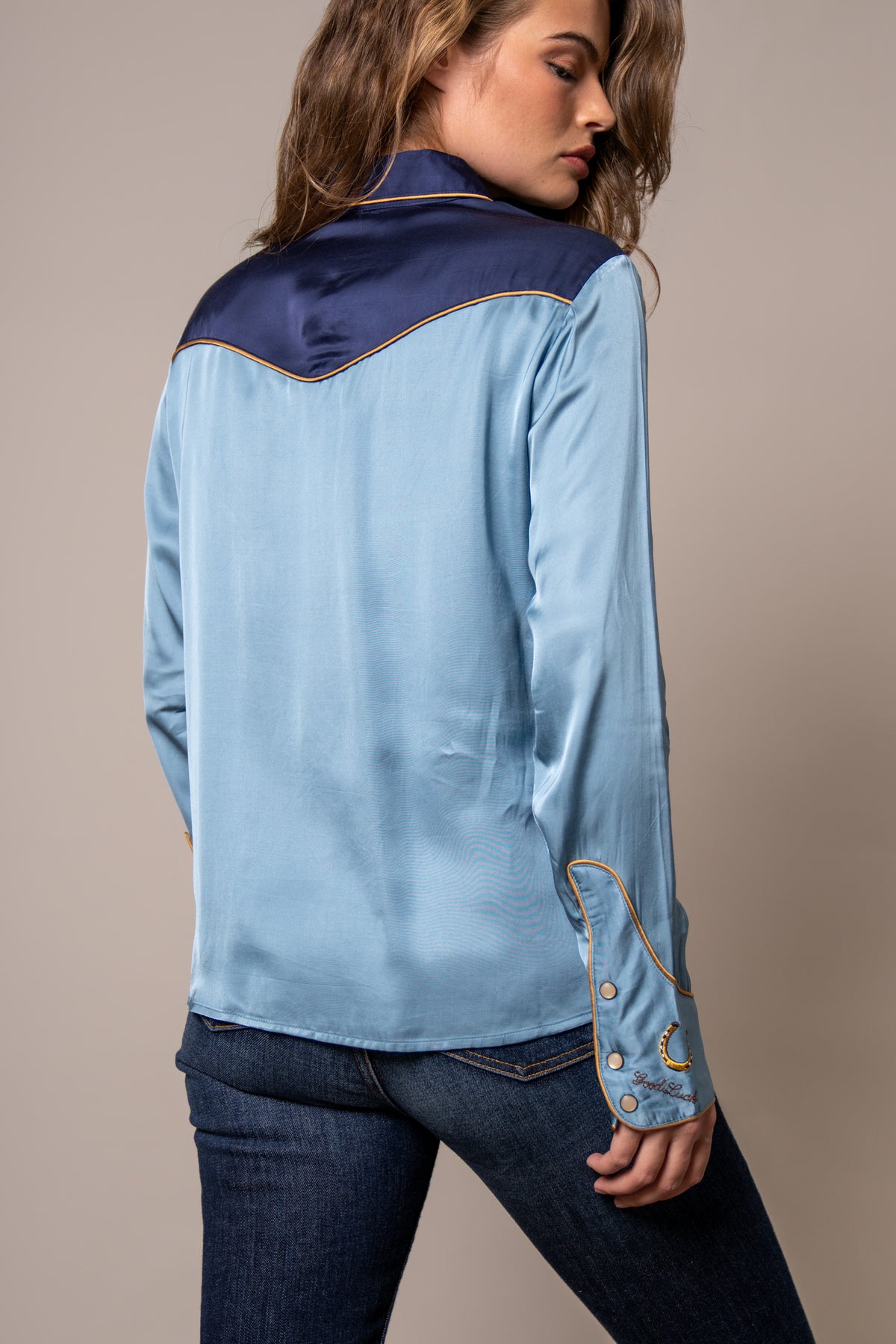 Kimes Ranch Merada top in Mid Blue, back view, with navy yoke and embroidered Good Luck horseshoe on the cuff