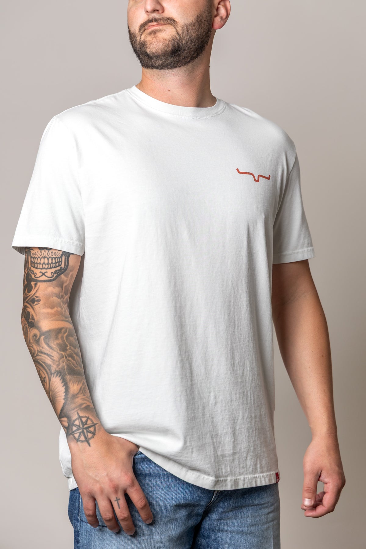 Kimes Ranch Not Our First shirt in Muted White with a small red Kimes Ranch logo on the chest