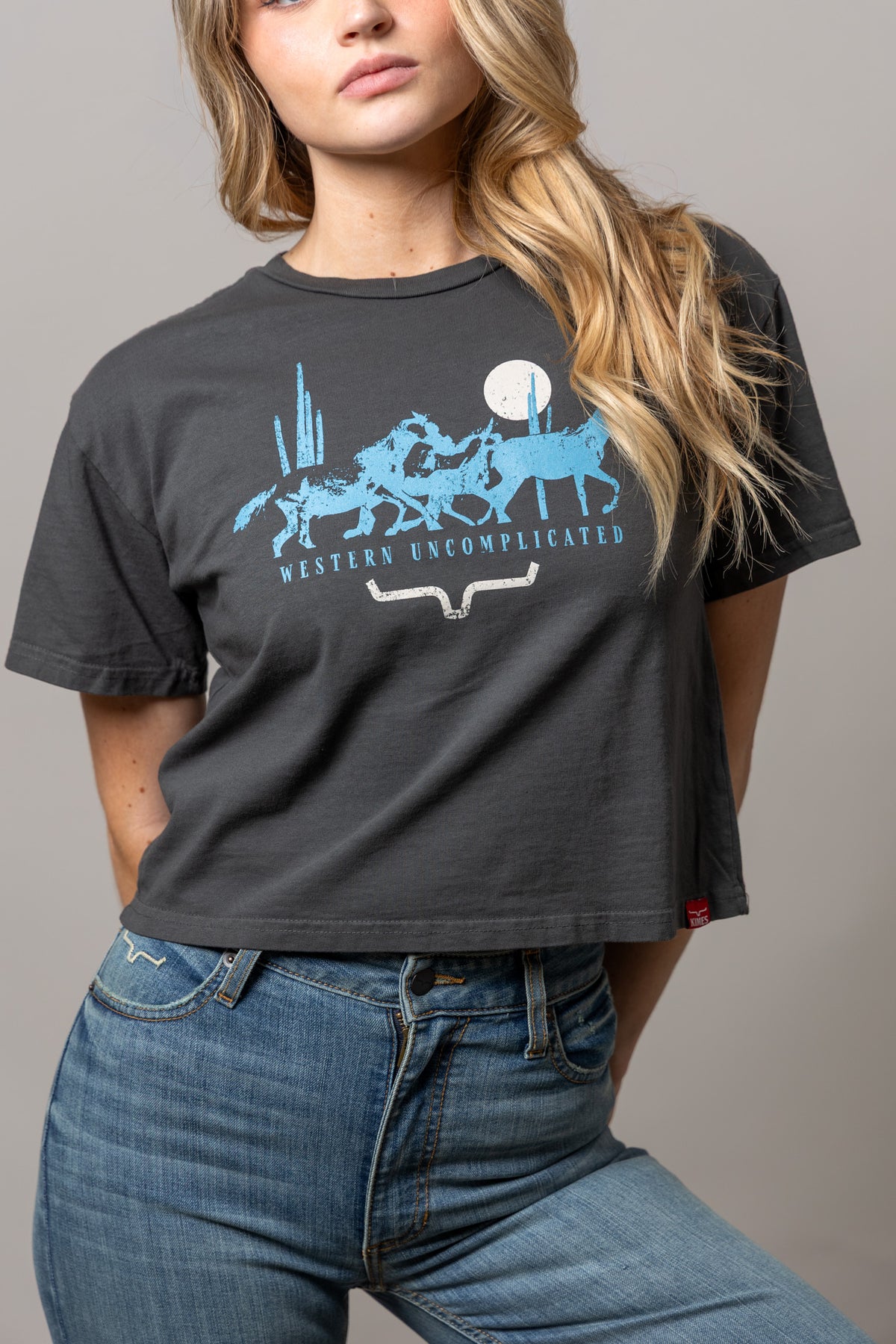 Kimes Ranch Plains Stampede shirt in Pepper with a blue graphic of horses and the text Western Uncomplicated