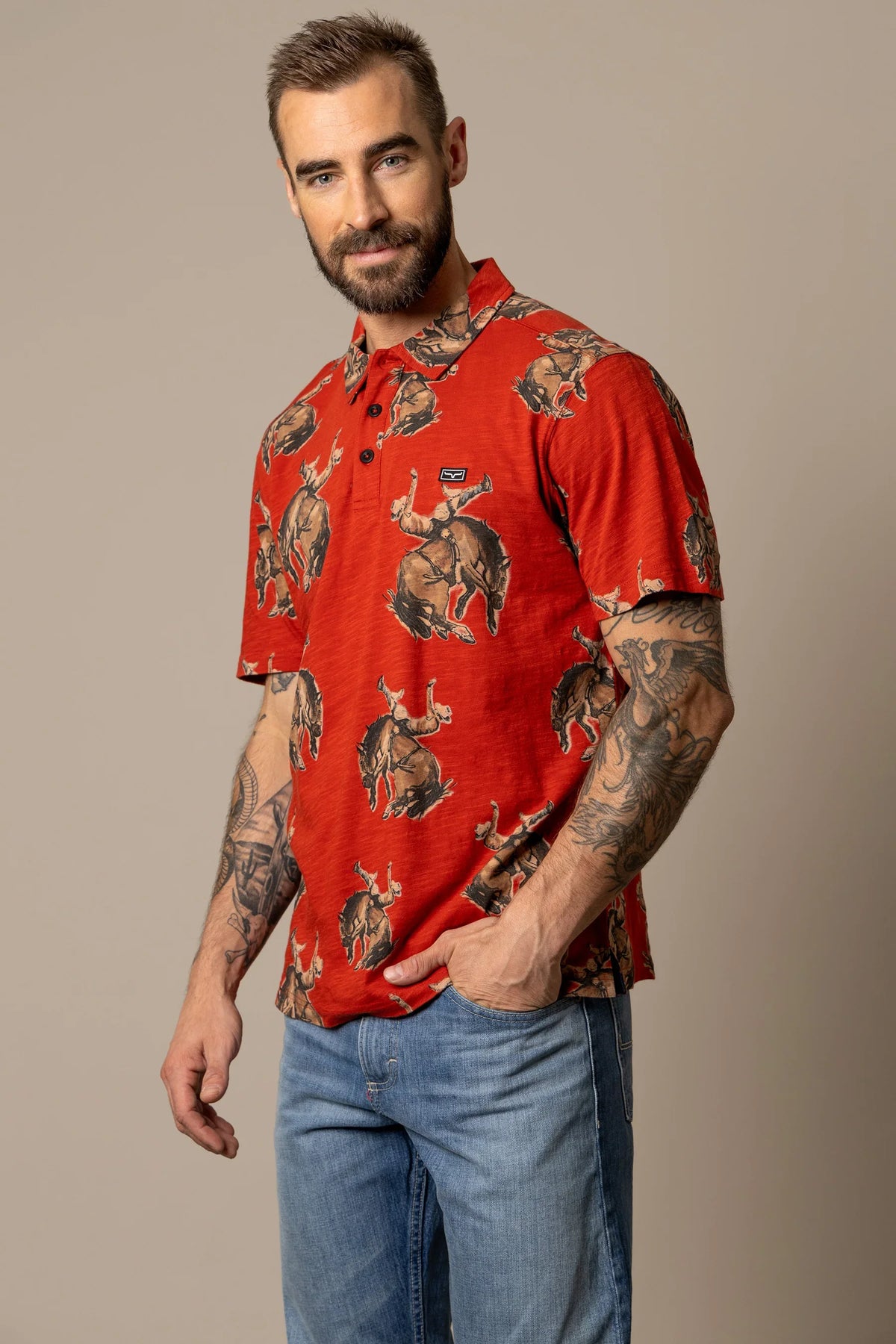 Kimes Ranch RP Winning Ride Polo in Brick Red with a repeating graphic of a cowboy riding a bucking bronco