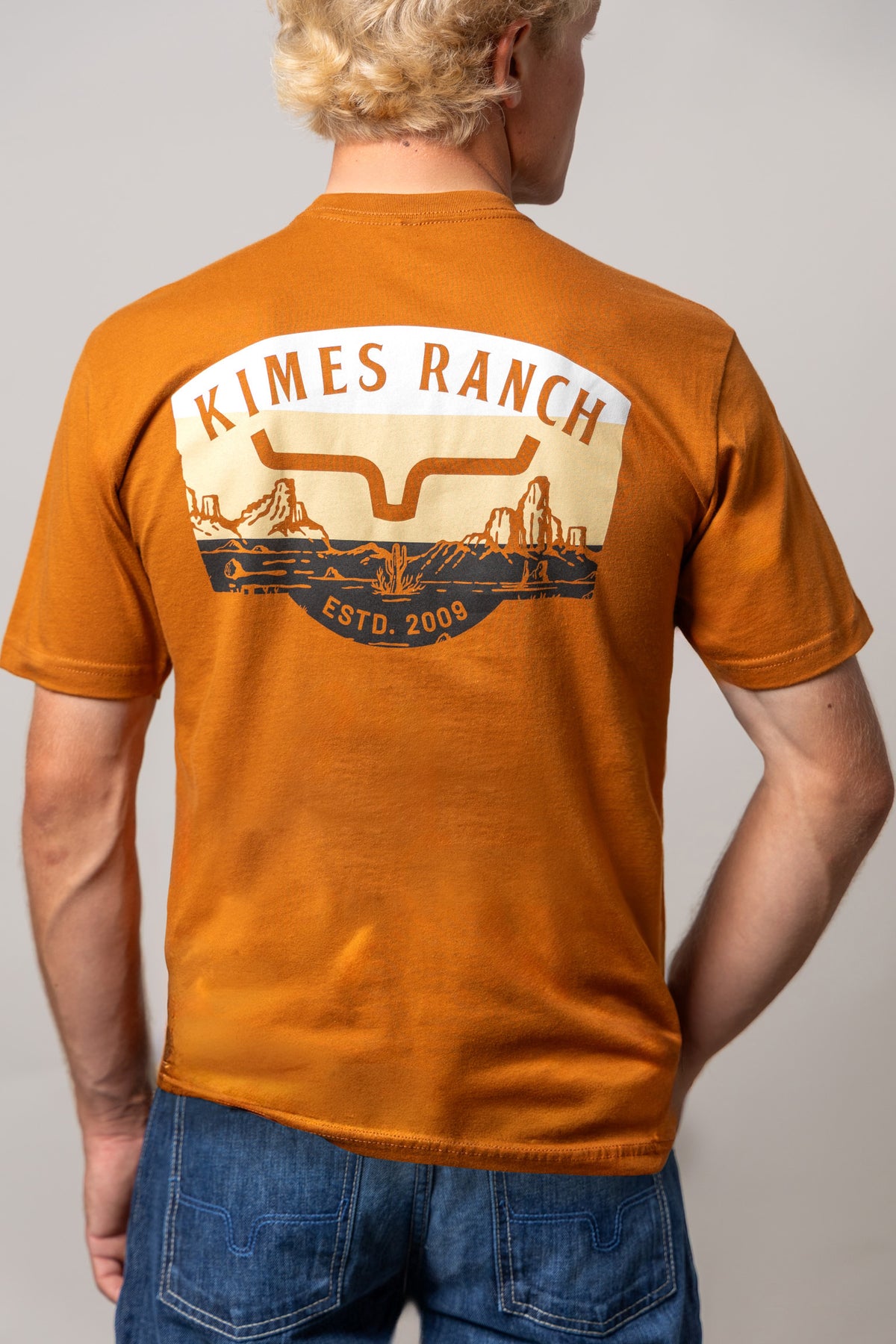 Kimes Ranch Southwestern shirt in Clay, back view, with a back graphic featuring a stylized steer logo and desert landscape