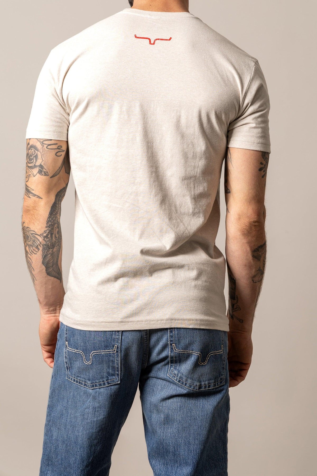 Kimes Ranch Stability shirt in Sand, back view, with short sleeves and a red Kimes Ranch logo at the back yoke