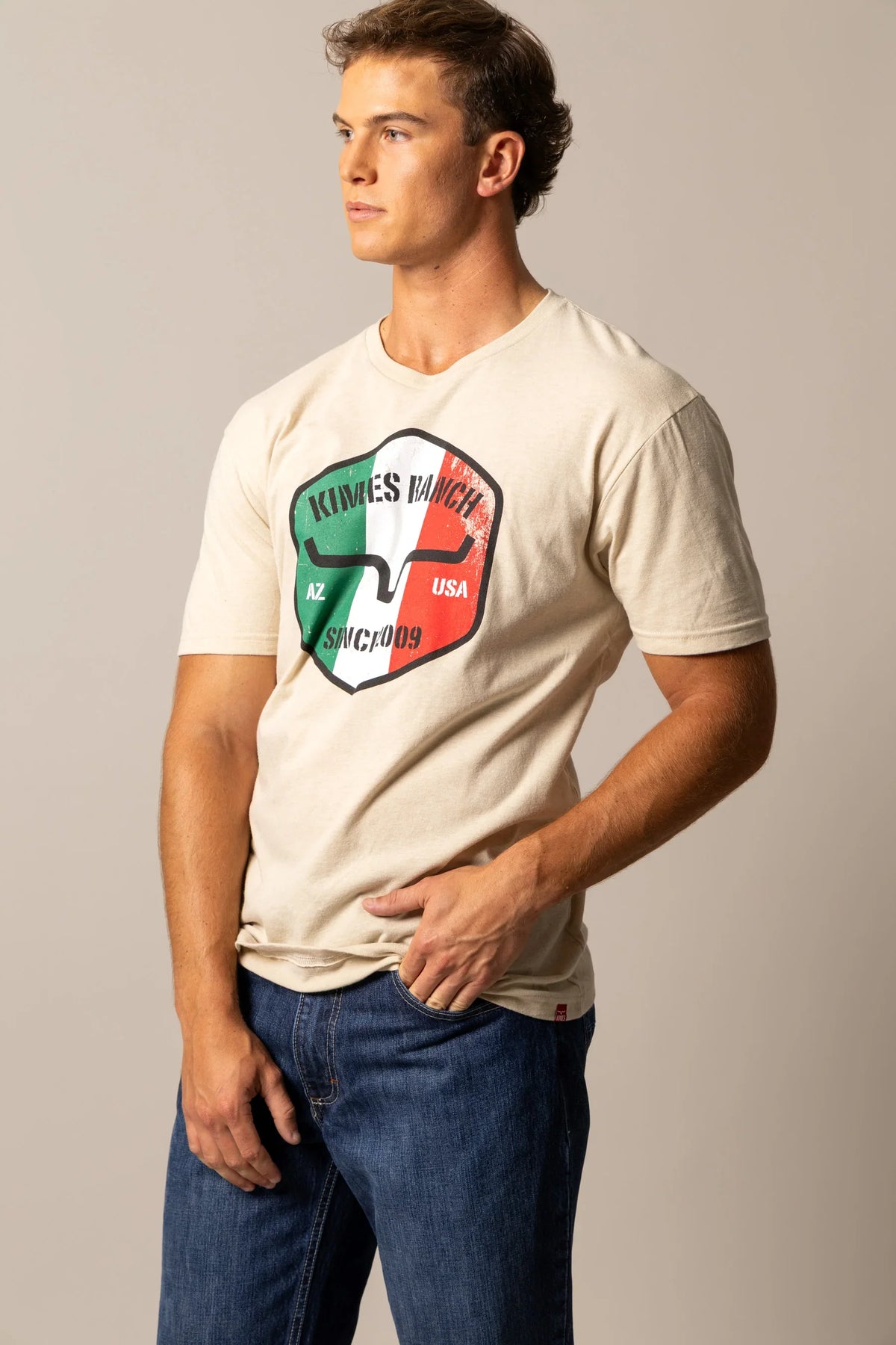 Kimes Ranch Triple Stripe shirt in Natural, side view, with shield graphic featuring Kimes Ranch logo