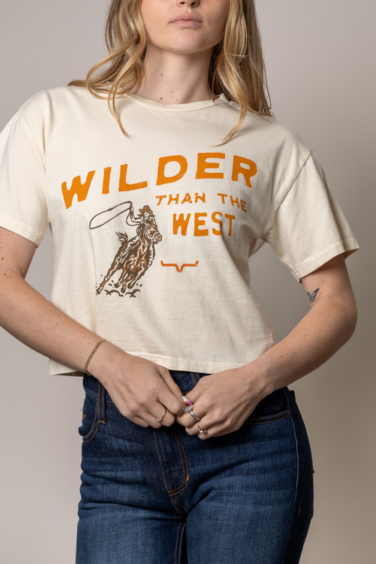 Kimes Ranch Wilder Than The West shirt in Ivory with a graphic of a cowboy on a horse and the text Wilder Than The West