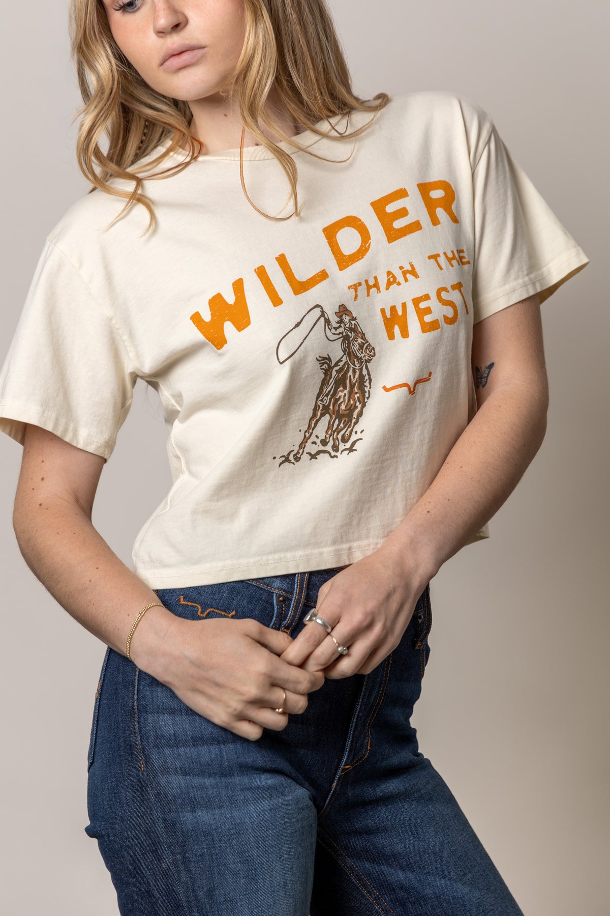 Kimes Ranch Wilder Than The West shirt in Ivory with a cowboy on horseback graphic and orange text