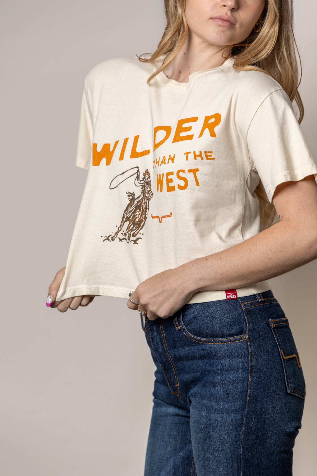 Kimes Ranch Wilder Than The West shirt in Ivory with a graphic of a cowboy on a horse and the text Wilder Than The West