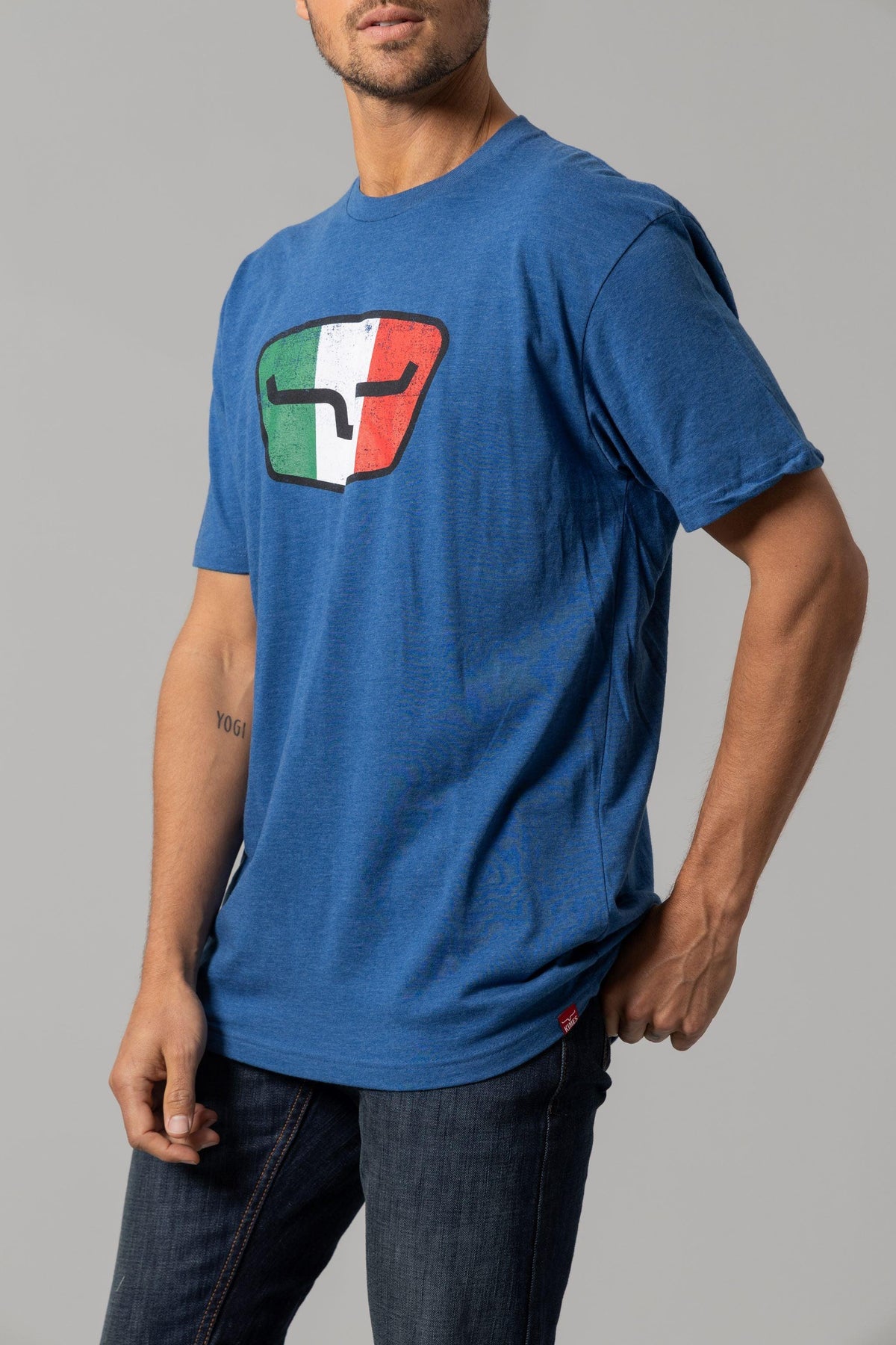 Kimes Ranch Tri-Color Tee in Heather Cool Blue with a shield graphic featuring green, white, and red vertical stripes