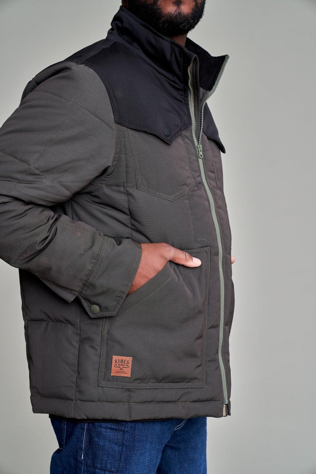Kimes Ranch Colt Jacket, side view, in charcoal with quilted sleeves, a black collar, and a logo patch on the front pocket