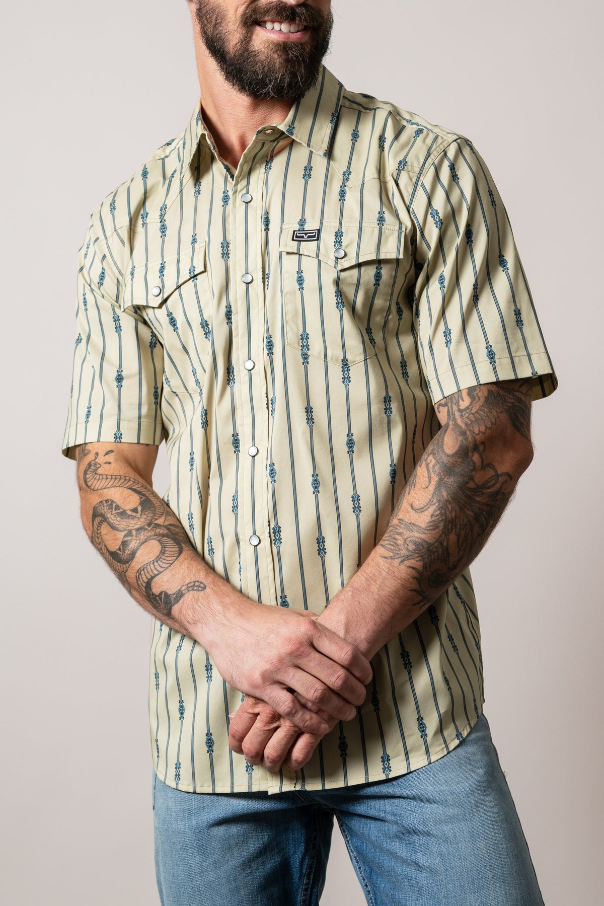 Kimes Ranch Gunner dress shirt in khaki with blue vertical stripes and two chest pockets, featuring Kimes Ranch logo