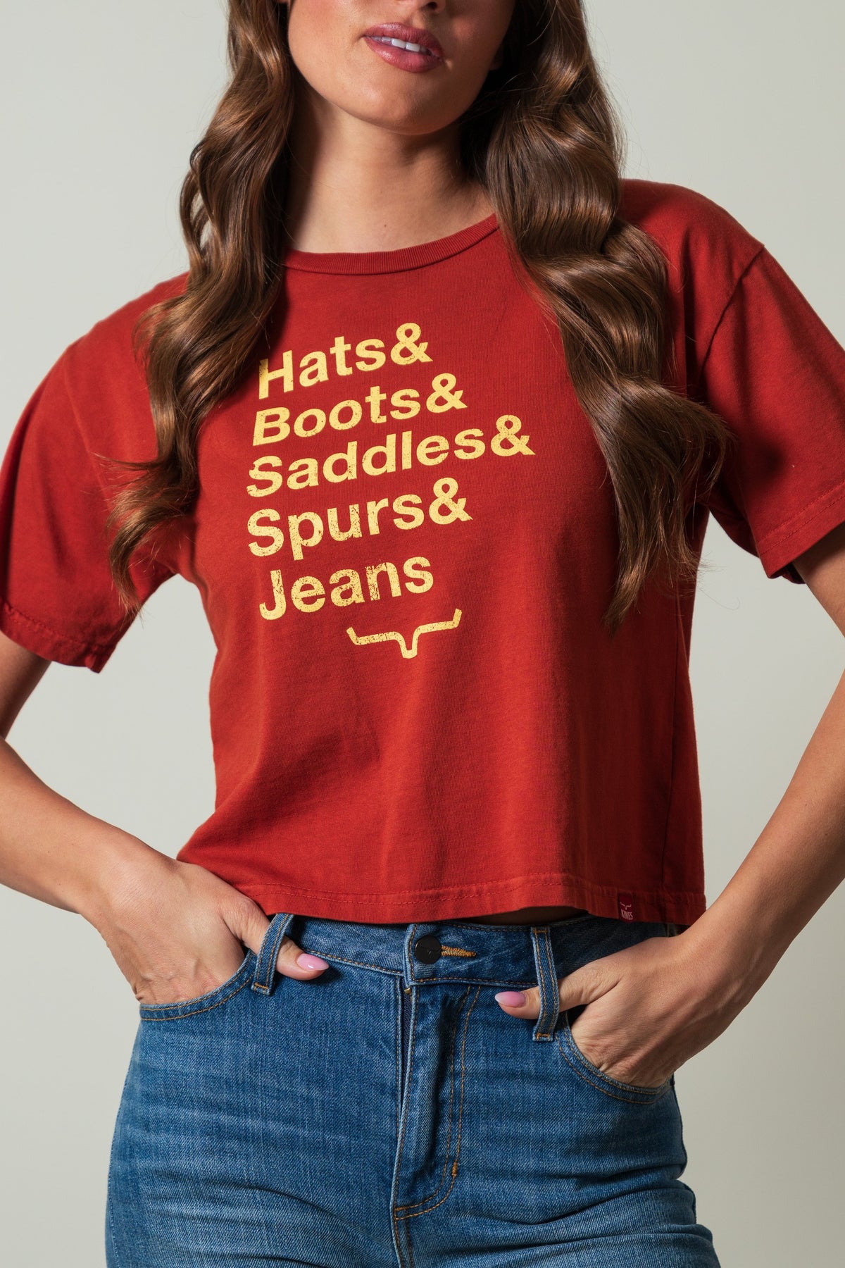 Kimes Ranch Hats & Boots shirt in Burnt Red with a gold screen print reading "Hats & Boots & Saddles & Spurs & Jeans"
