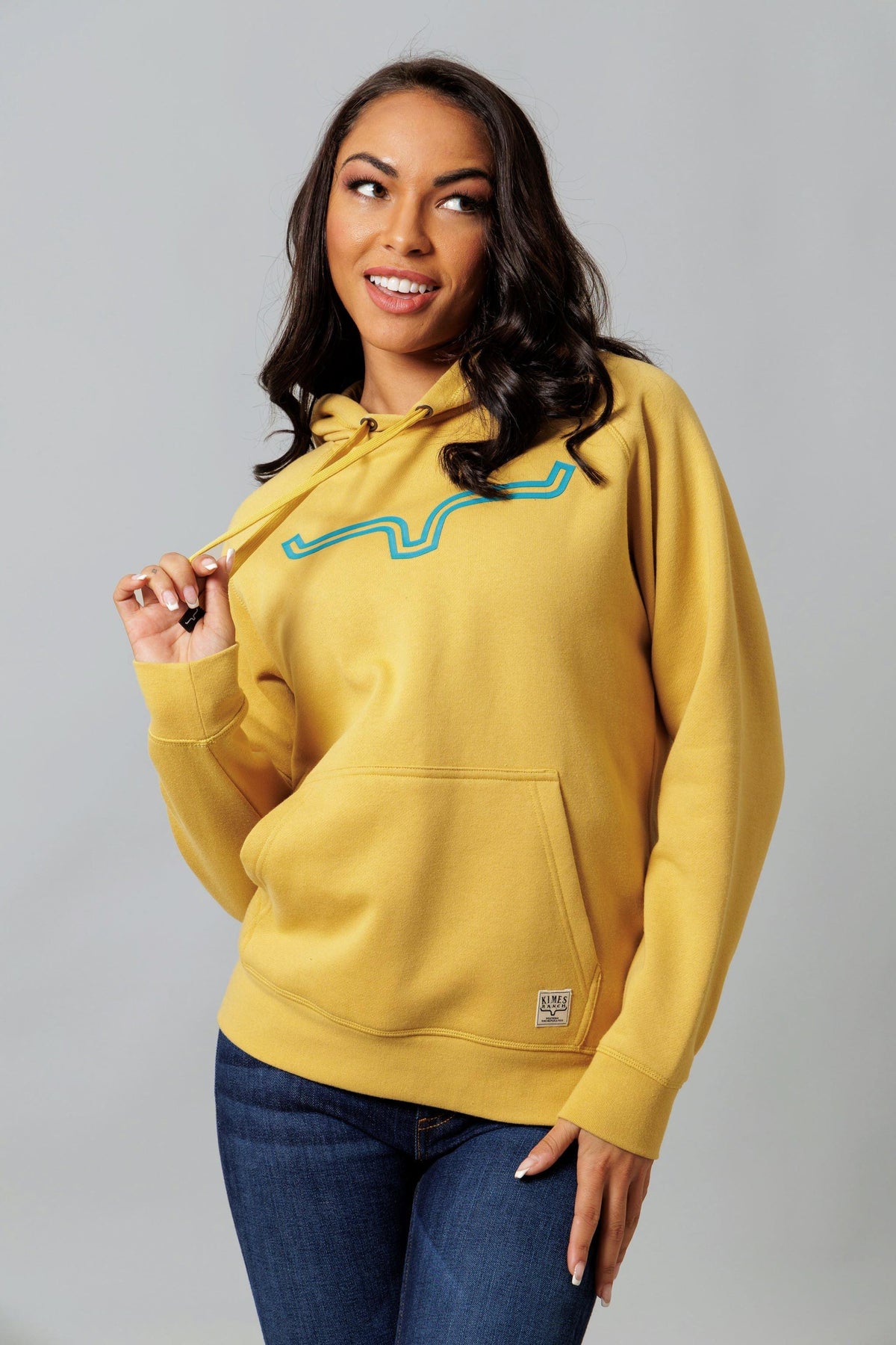 Kimes Ranch Ladies Outlier Hoodie in Gold with a blue graphic and front kangaroo pocket
