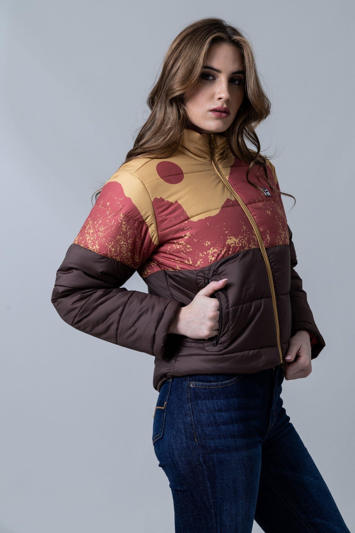 Kimes Ranch Valencia Puffy jacket in Gold, side view, with a mountain graphic and brown lower panel