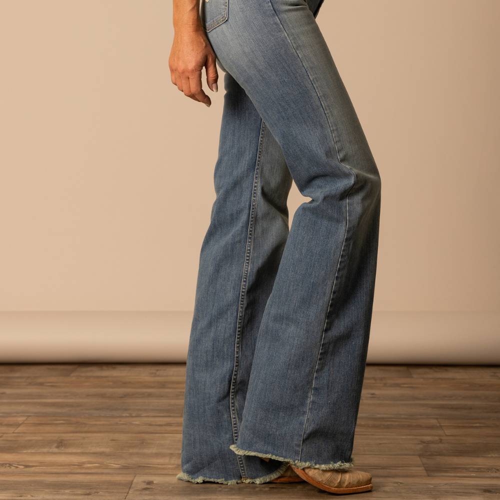 Woman wearing Kimes Ranch Olivia jeans in a cool-toned light wash with a high-rise fit, wide leg, and raw hem. The jeans feature horn logos on both back pockets and a soft sage undertone for a modern Western look.