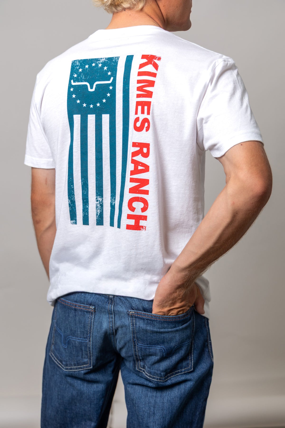 Kimes Ranch 76, back view, White short sleeve shirt with a teal flag graphic and red KIMES RANCH text on the back