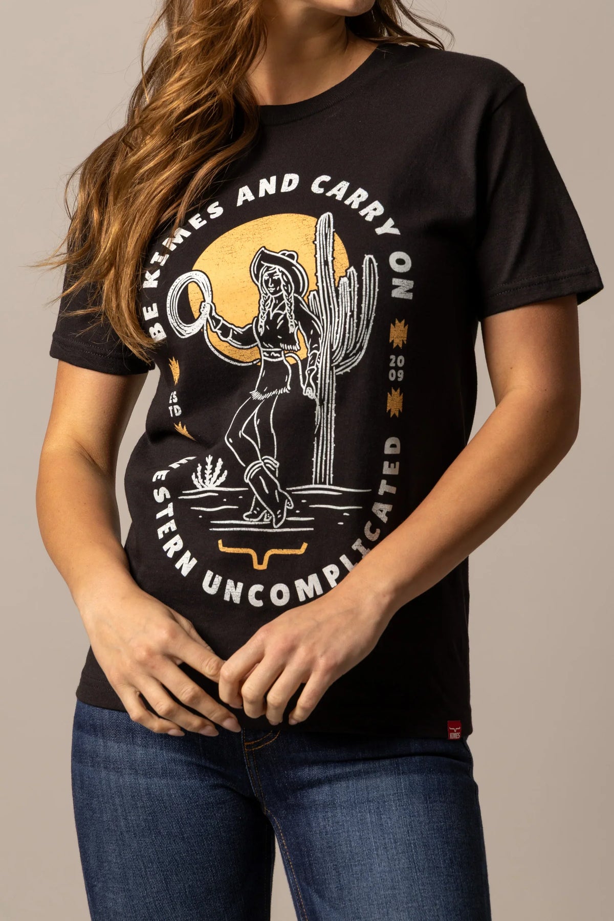 Kimes Ranch Be Kimes shirt in Black with a graphic of a cowgirl and the text "BE KIMES AND CARRY NO WESTERN UNCOMPLICATED"
