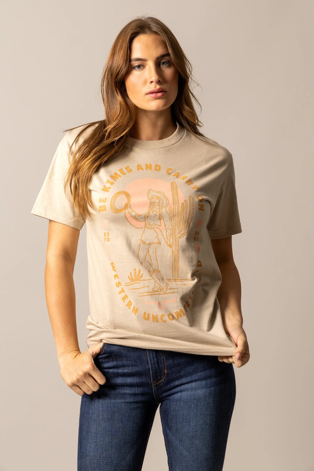 Kimes Ranch Be Kimes shirt in Sand with a graphic of a cowgirl and text reading Be Kimes and Carry On