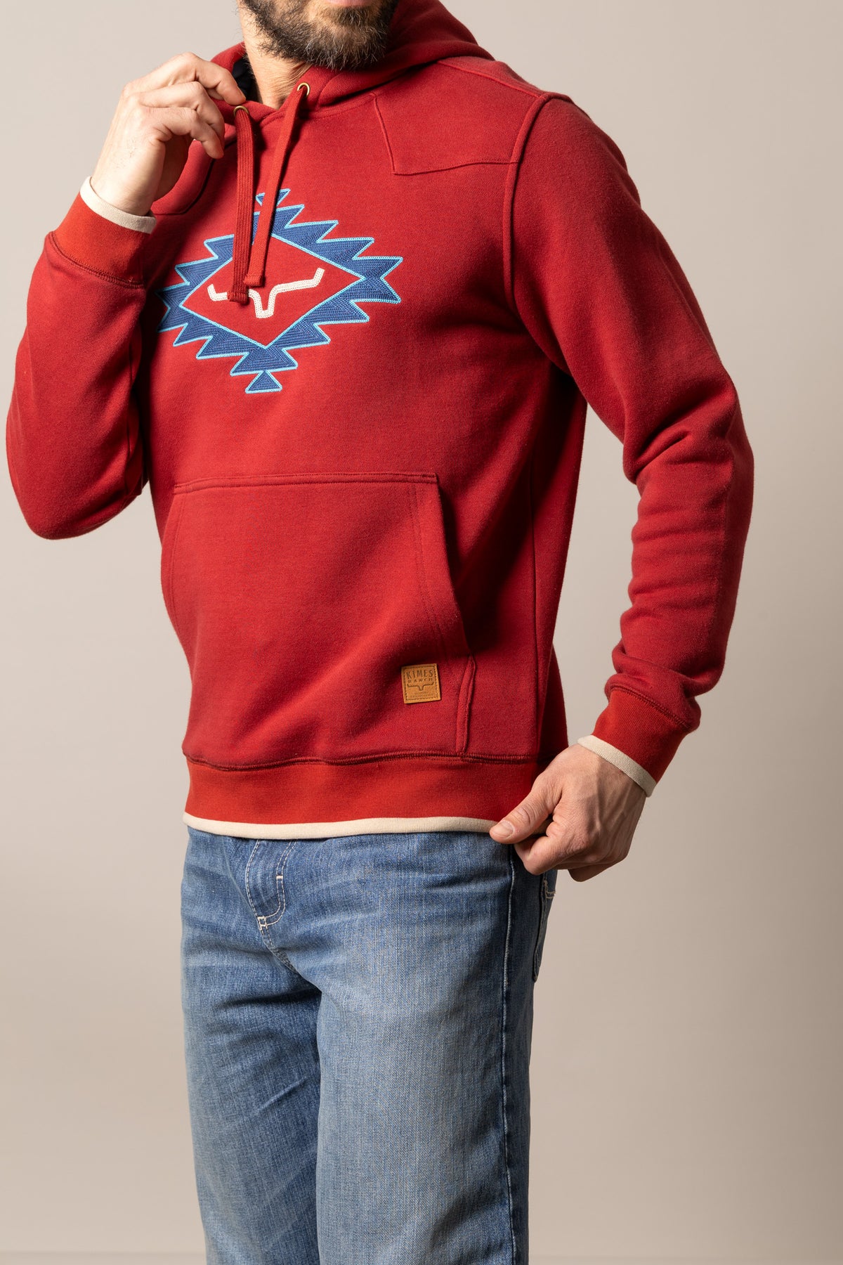 Kimes Ranch Berger hoodie in Brick Red with a blue and white embroidered graphic on the chest and a front kangaroo pocket