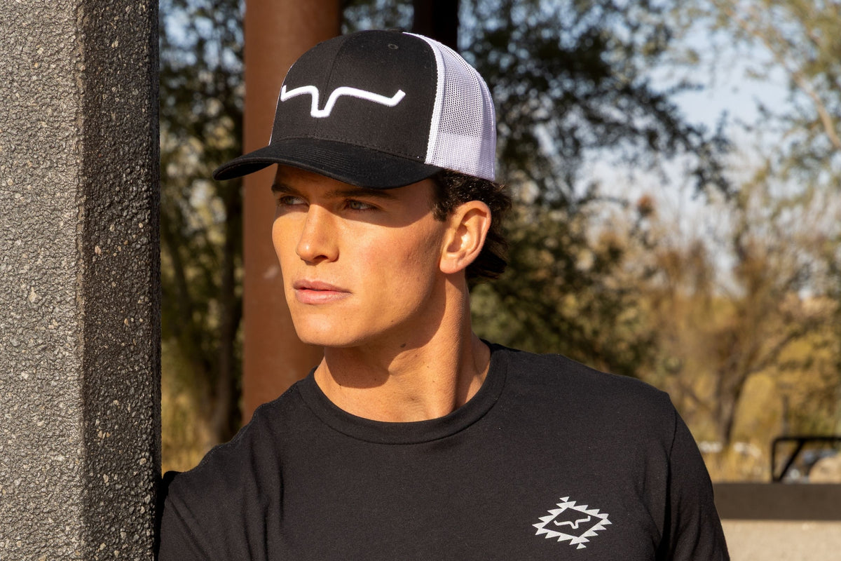 Kimes Ranch Weekly Trucker Hat in Black White with a white logo on the front