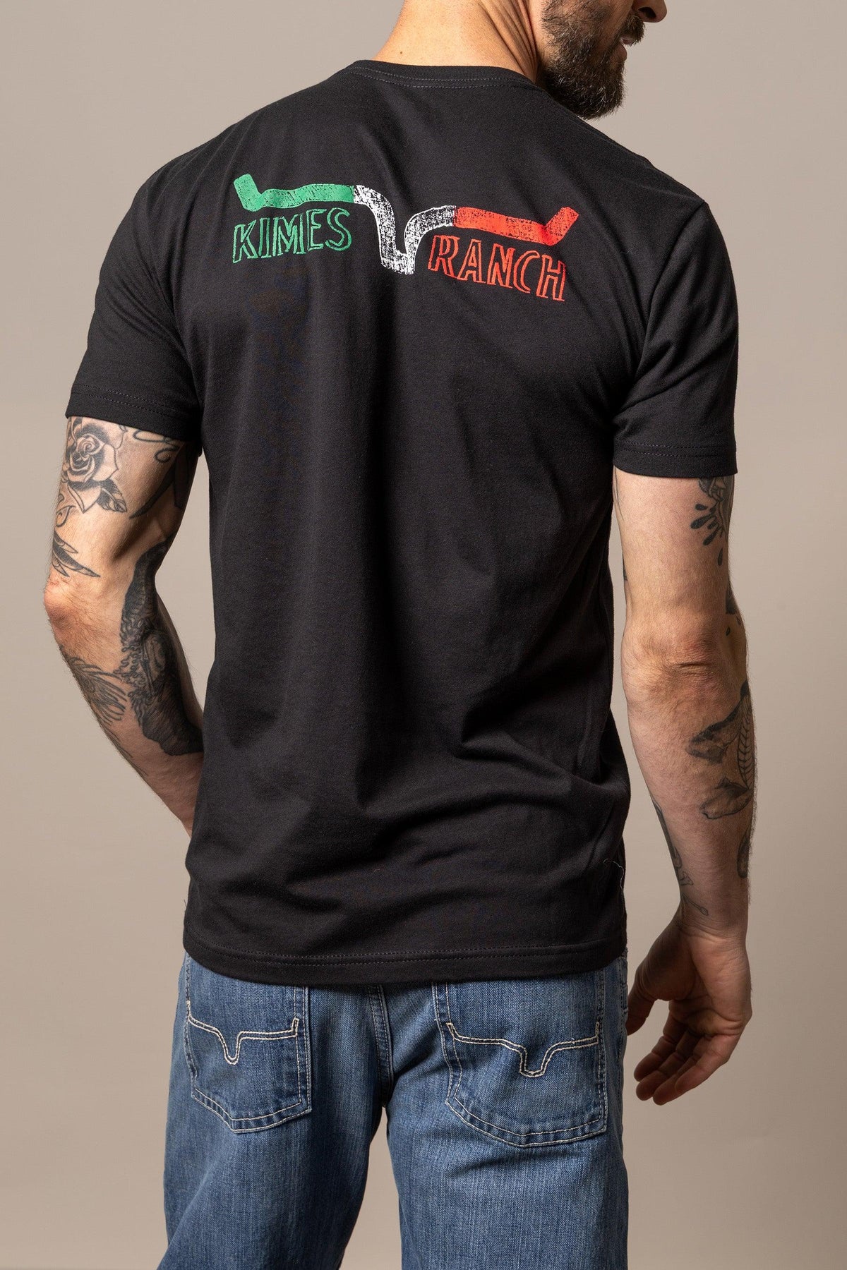 Kimes Ranch Dibujada, back view, Black shirt with KIMES RANCH text in green and red with a white swoosh