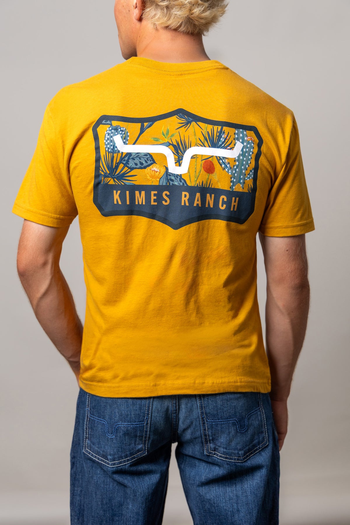 Kimes Ranch Dillard Floral shirt in Antique Gold, back view, with a back graphic of desert plants and the Kimes Ranch logo