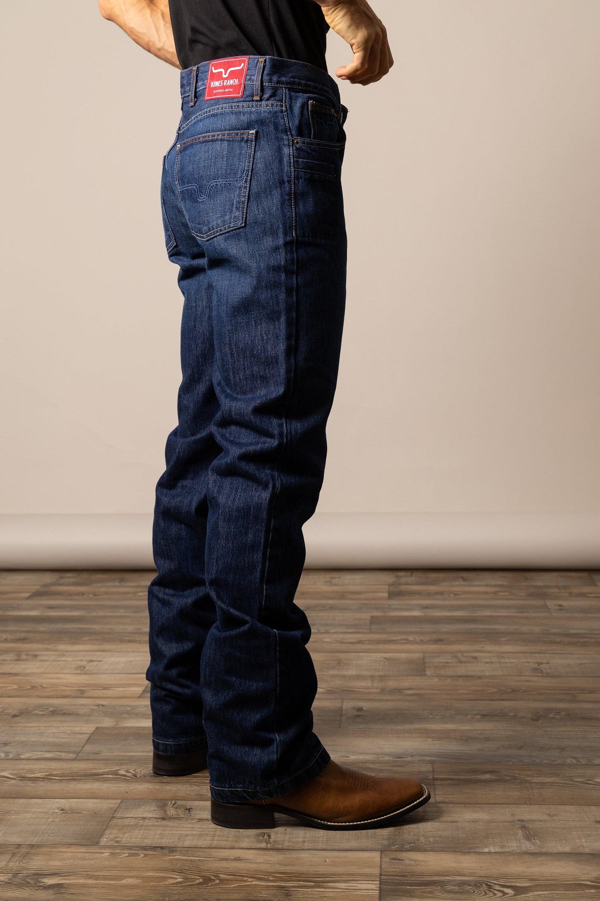 Kimes Ranch Dillon Relaxed Bootcut jeans in Dark Wash, side view, with back pockets and red logo patch