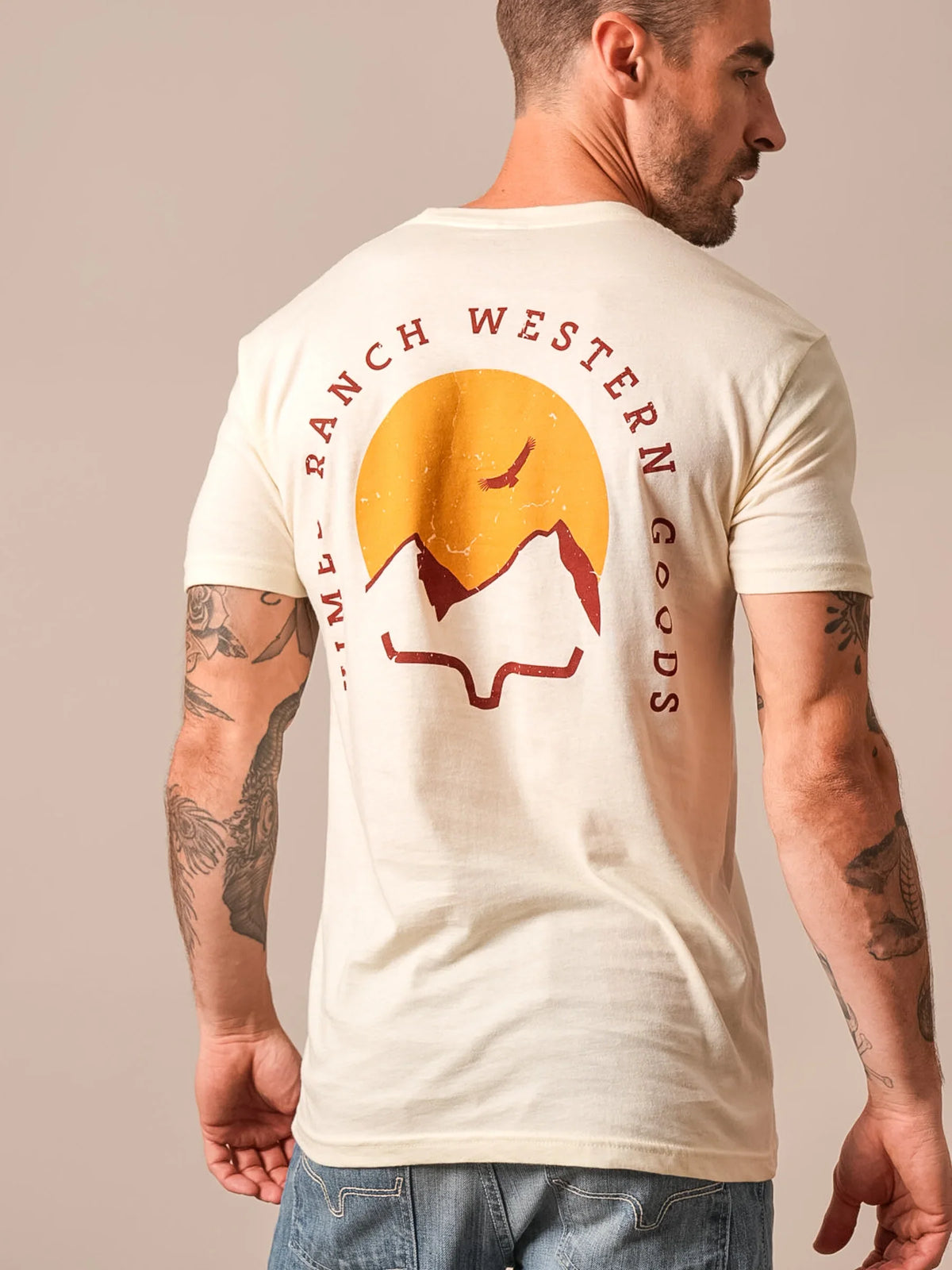 Kimes Ranch Flying High shirt in Natural, back view, with a back graphic of a sun, mountains