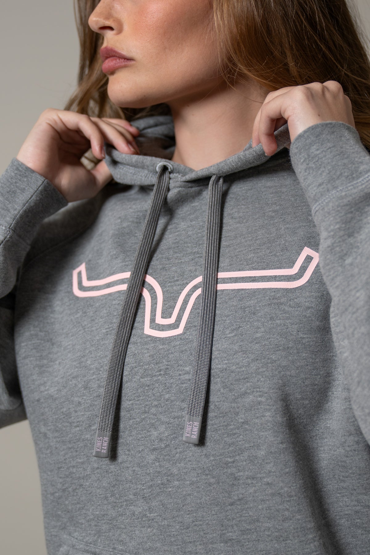 Kimes Ranch Ladies Outlier Hoodie in Grey Heather, close-up, with a pink Kimes Ranch logo and drawstring aglets