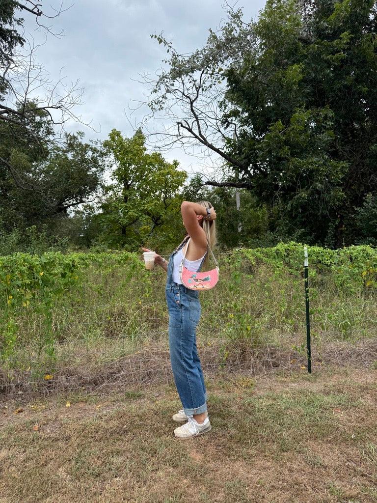 Kimes Ranch Billy Overalls, side view, in blue with rolled cuffs and a pink embroidered bag