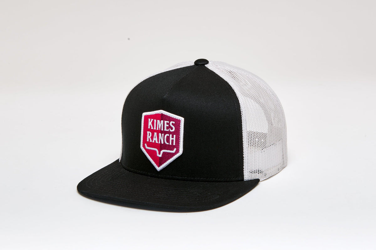 Kimes Ranch Jack Trucker Hat in Black, side view, with a red and white shield logo on the front and white mesh back