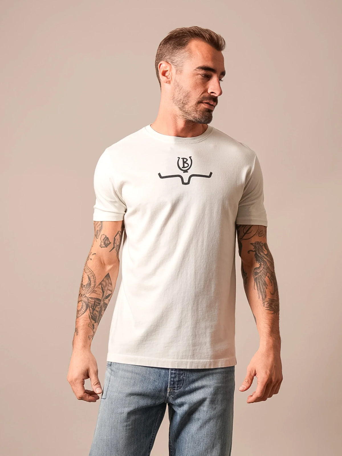 Kimes Ranch Lucky B Saddle shirt in Natural with a short sleeve crew neck and a black logo graphic on the chest