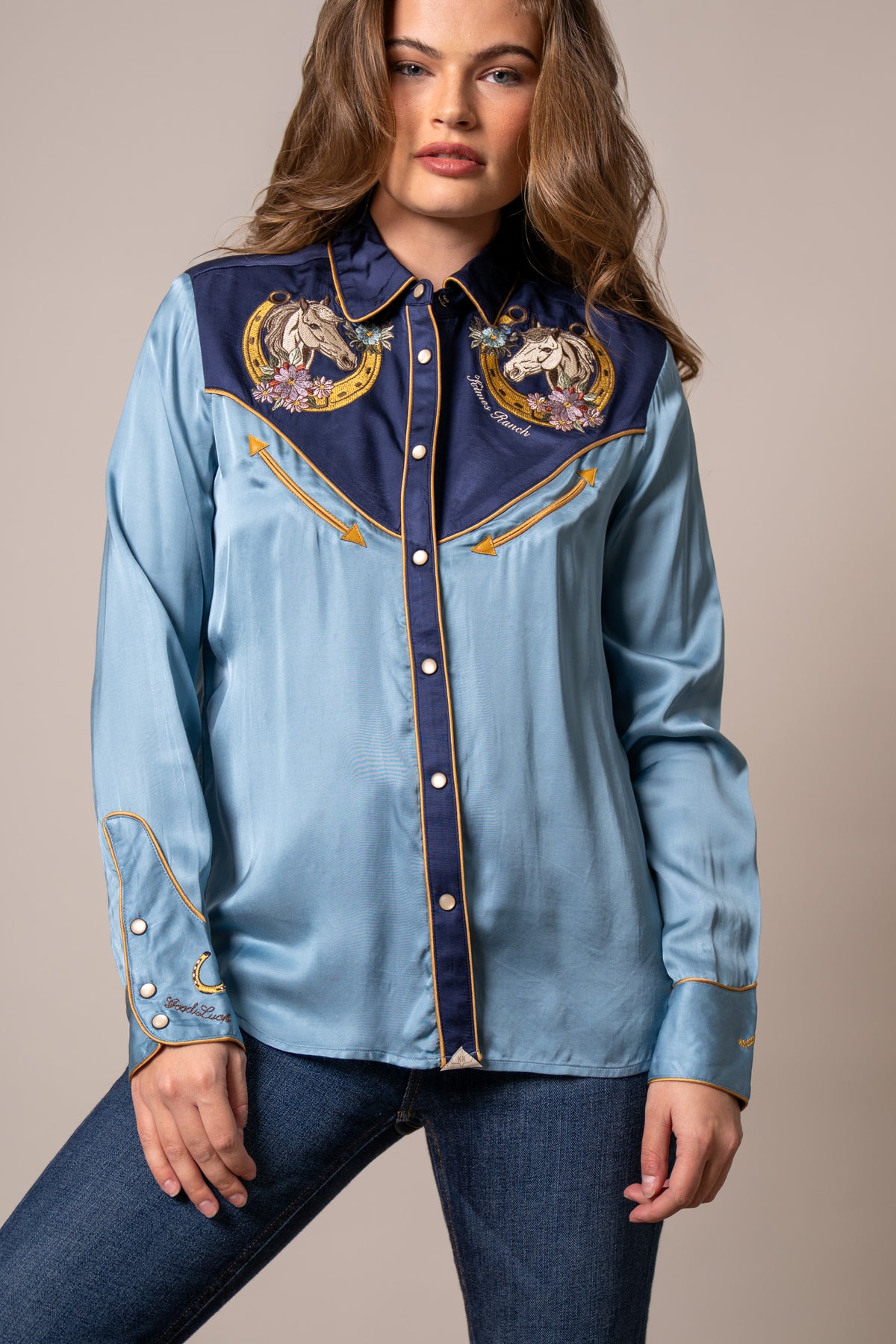 Kimes Ranch Merada top in Mid Blue with embroidered horse heads on the yoke and gold piping