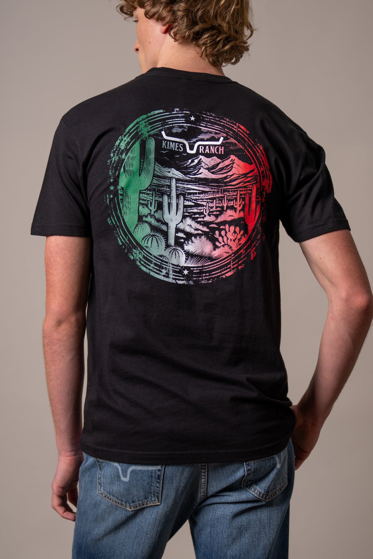 Kimes Ranch Mexico Prairie shirt in Black, back view, with a large back graphic of a desert landscape and cacti in green