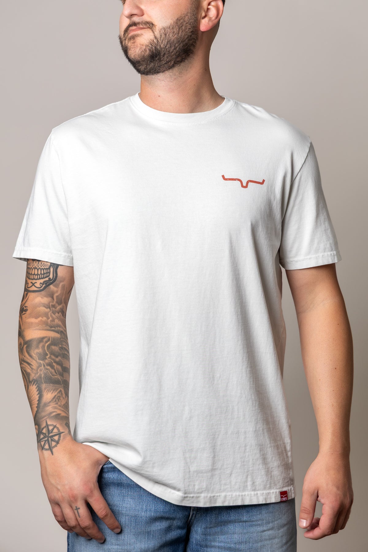 Kimes Ranch Not Our First shirt in Muted White with a small orange Kimes Ranch logo on the chest