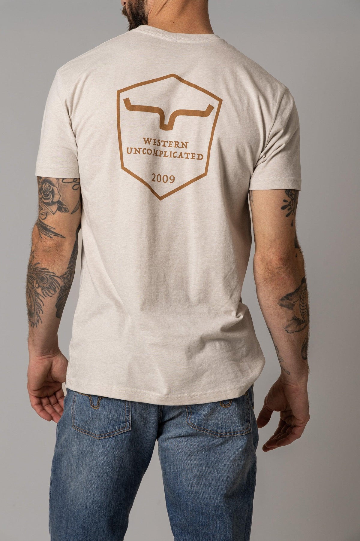 Kimes Ranch Shielded Trucker Shirt in Sand, back view, with back Kimes Ranch logo and Western Uncomplicated 2009 text