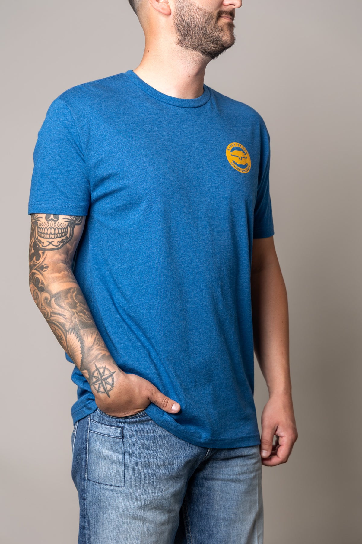 Kimes Ranch Wood Stamp shirt in Heather Cool Blue, side view, with a yellow circular logo on the chest