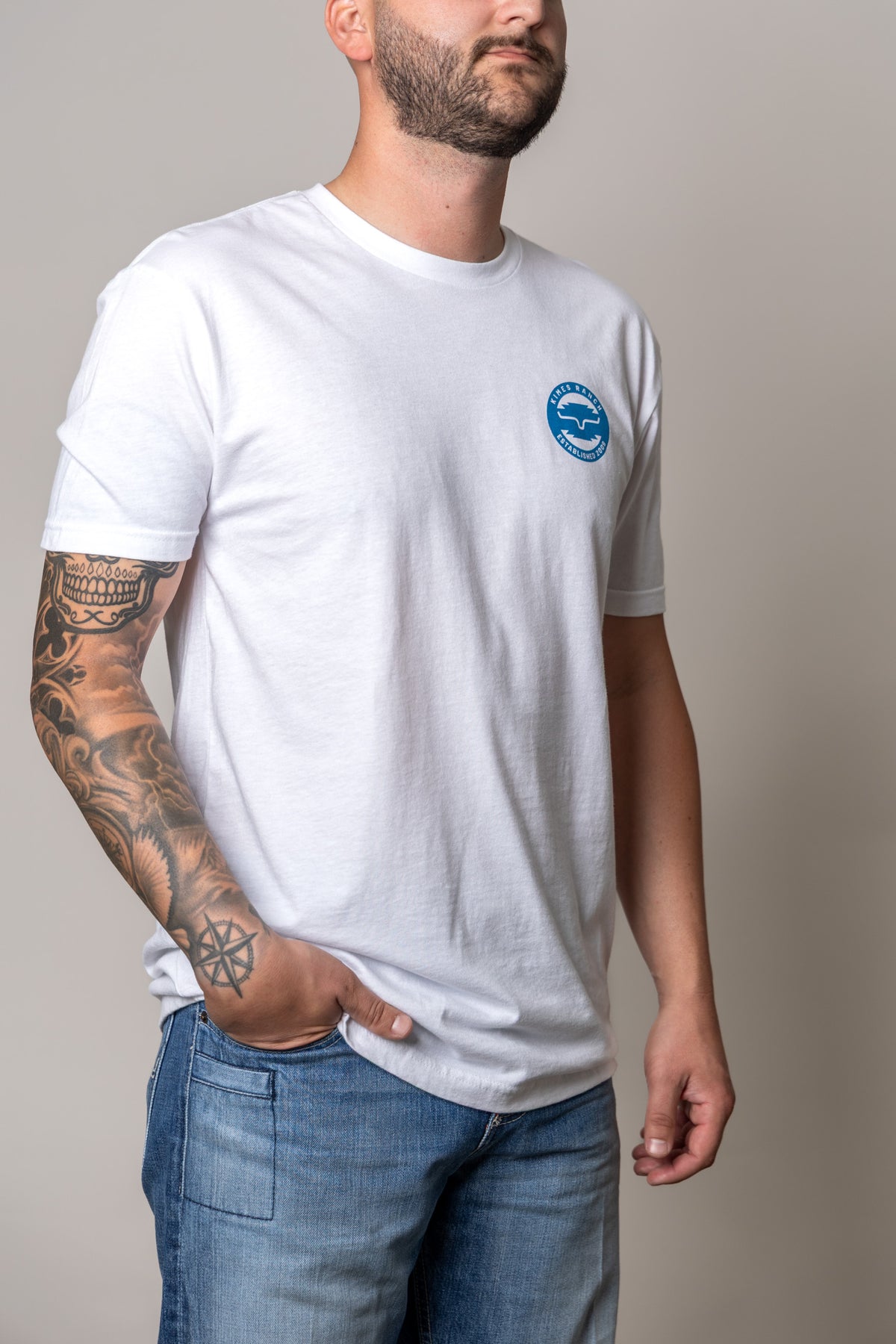 Kimes Ranch Wood Stamp shirt in White, side view, with a blue circular logo on the chest