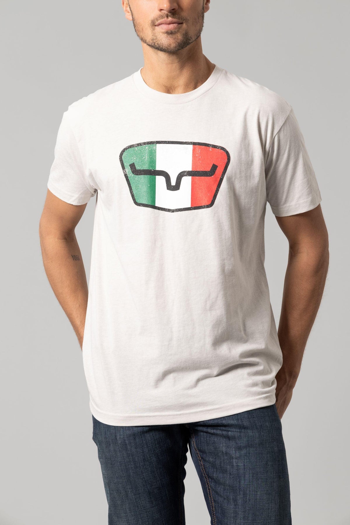 Kimes Ranch Tri-Color Tee in Sand with a distressed shield graphic featuring green, white, and red vertical stripes