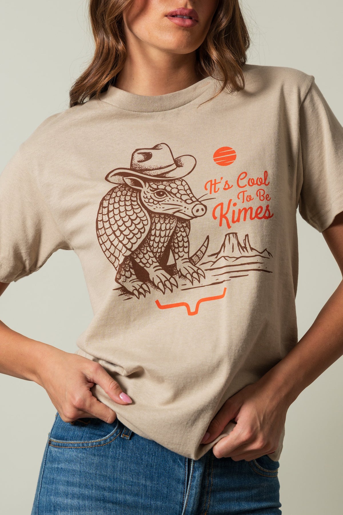 Kimes Ranch Dillo shirt in Sand, featuring an armadillo in a cowboy hat with "It's Cool To Be Kimes" text and orange accents