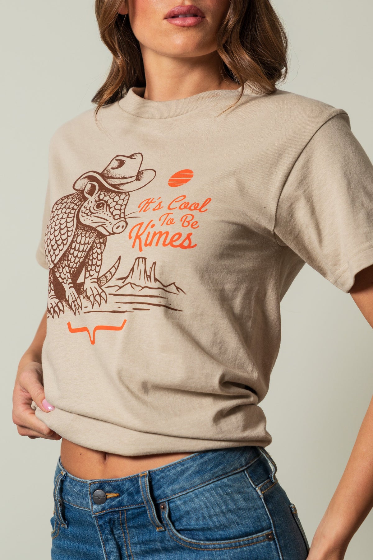 Kimes Ranch Dillo shirt in Sand, featuring a long-sleeve tee with a graphic of an armadillo wearing a cowboy hat and the text